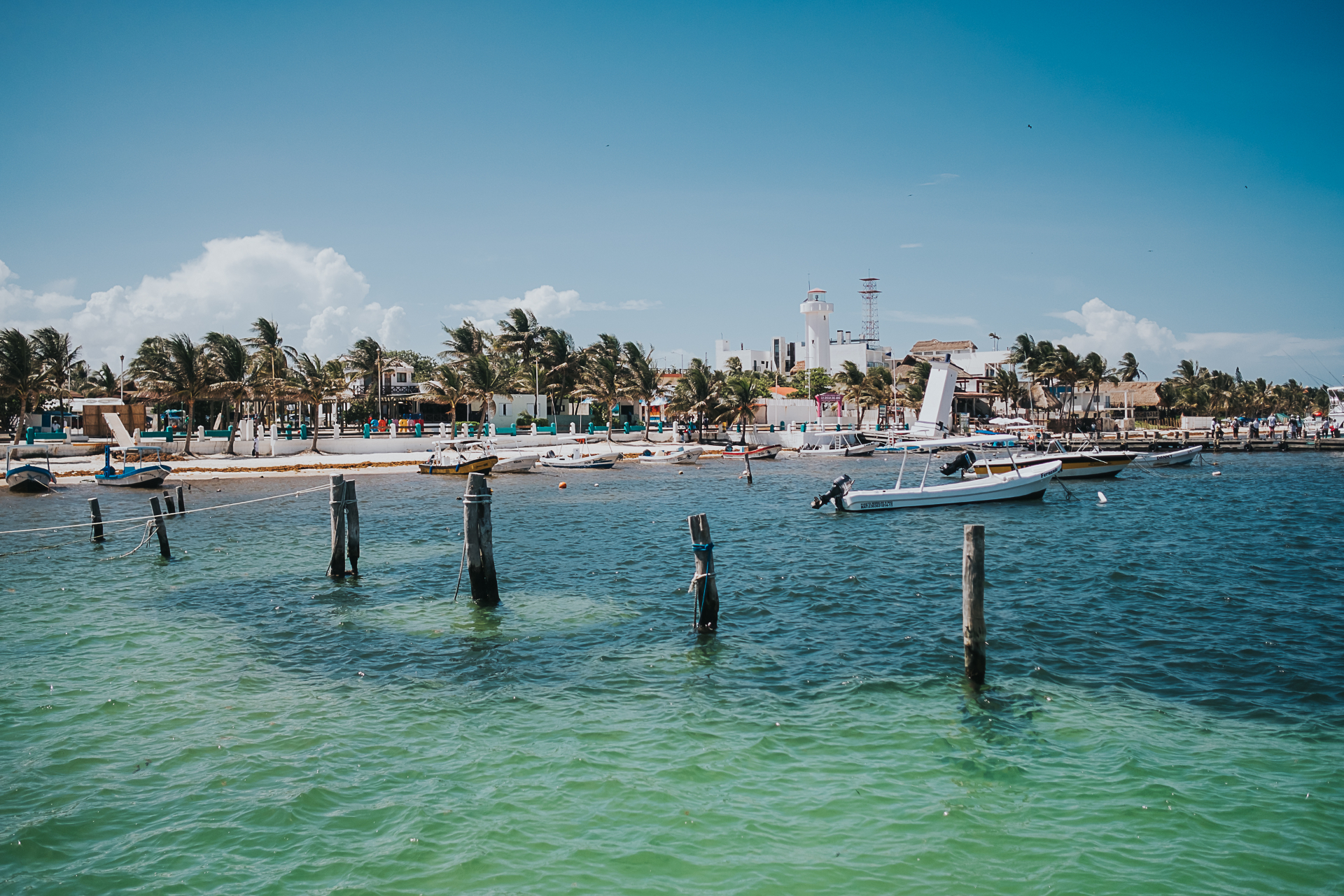 Puerto Morelos waterfront seen from the water, with the leaning lighthouse, palm trees and moored fishing boats