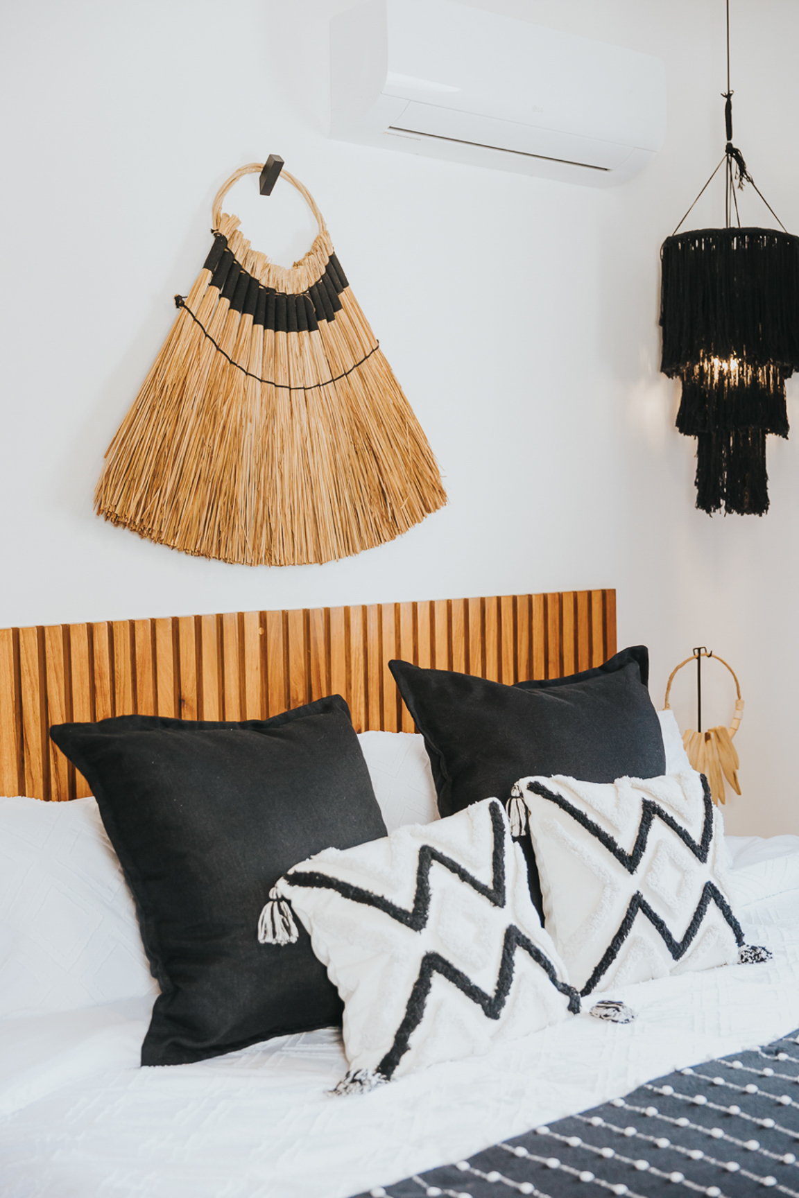 Bedroom detail with slatted wood headboard, palm fan and macramé pendant
