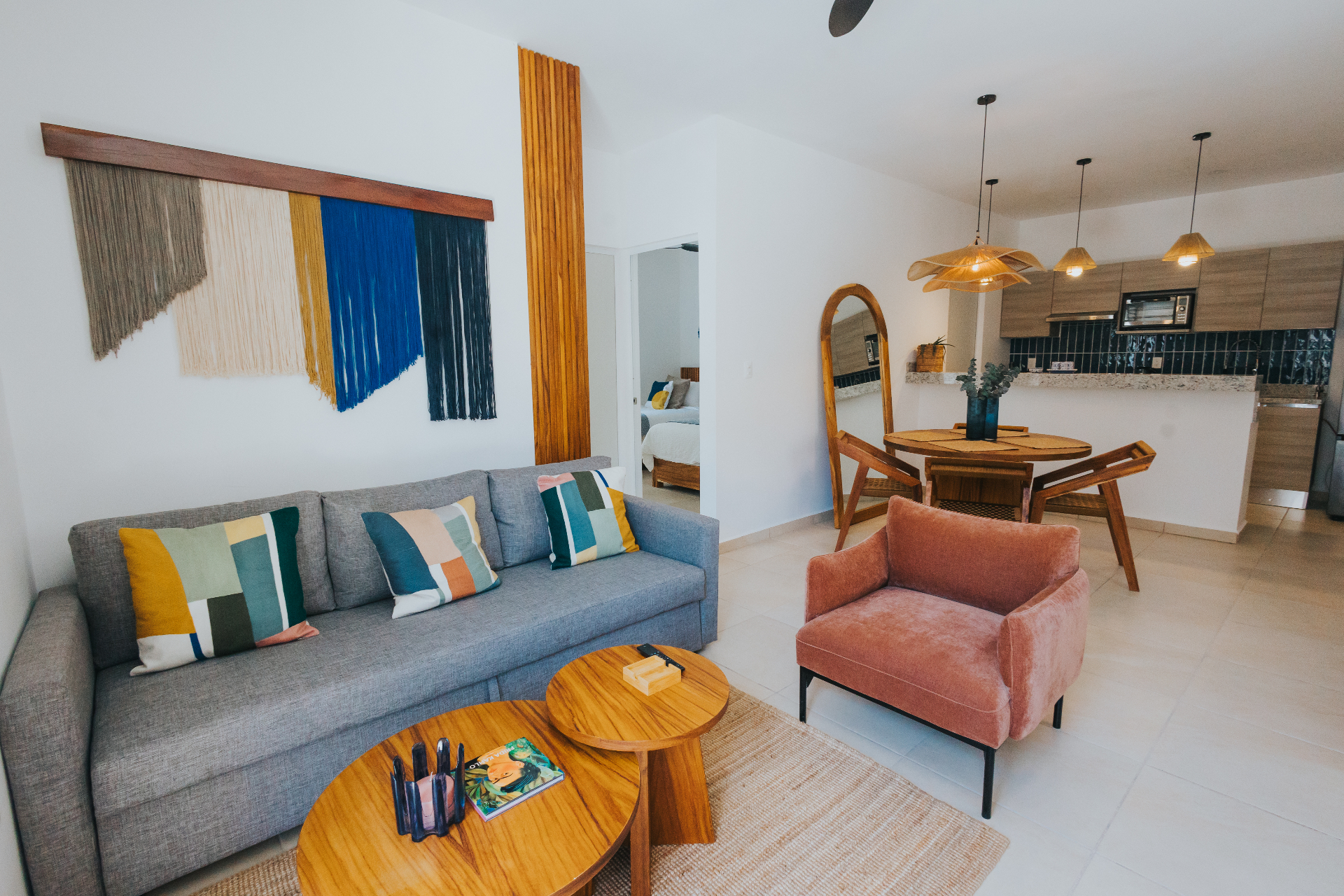 Open living room with grey sofa, coral velvet armchair, geometric cushions and indigo macramé wall art