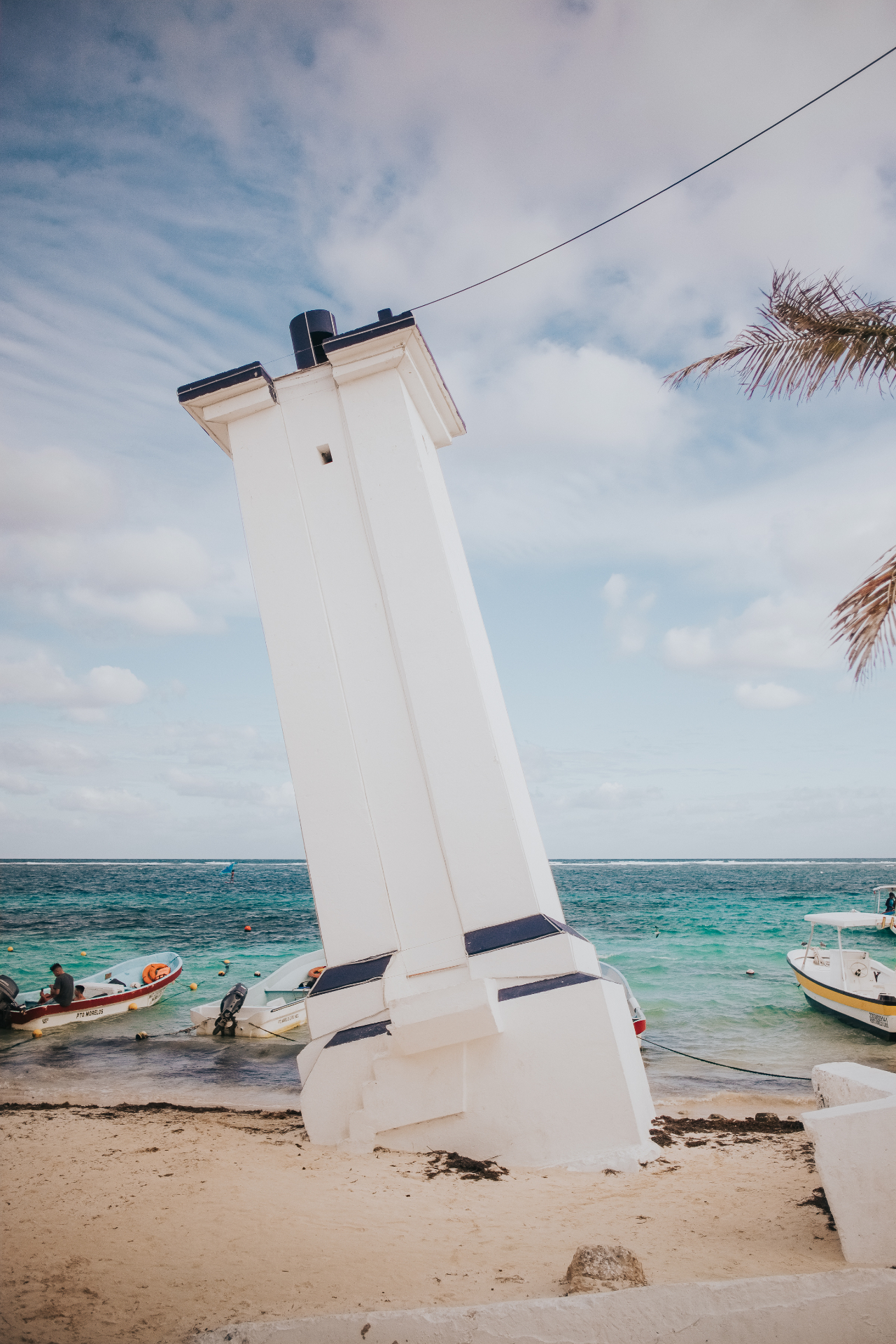 The leaning lighthouse of Puerto Morelos beside fishing boats and the Caribbean